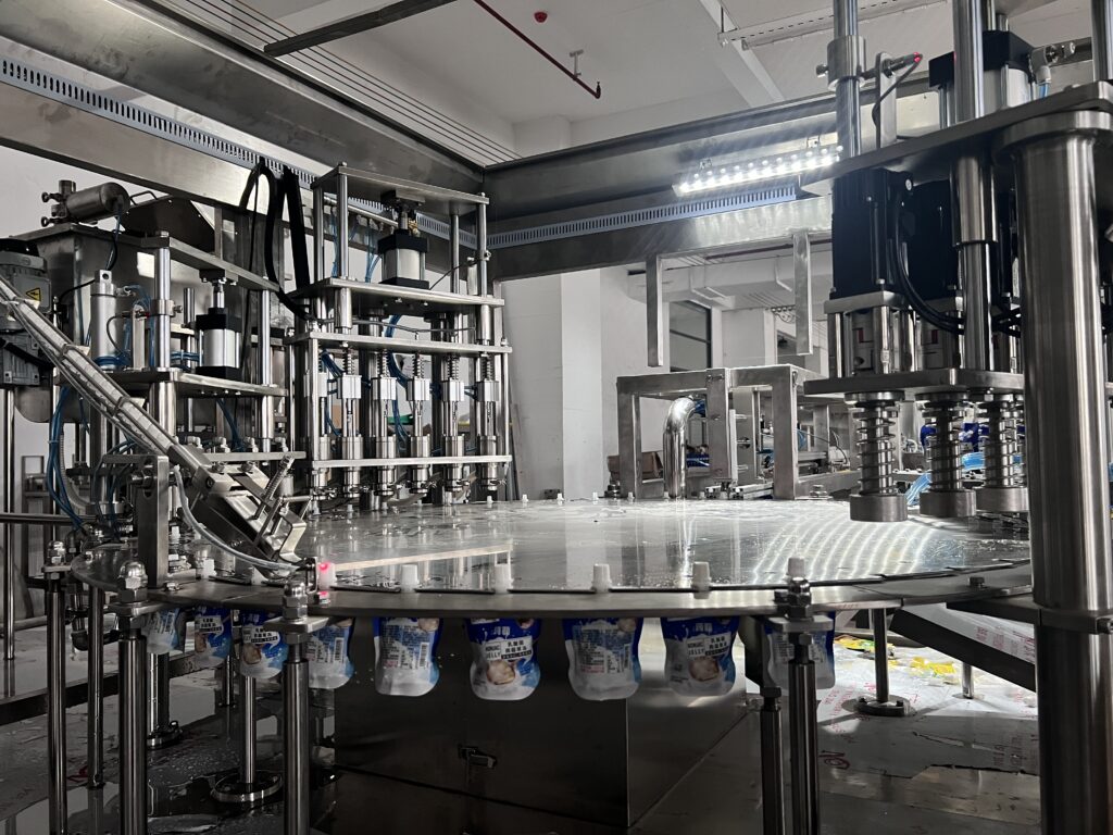 A worker operating a spout pouch filling and capping machine in a clean factory environment.