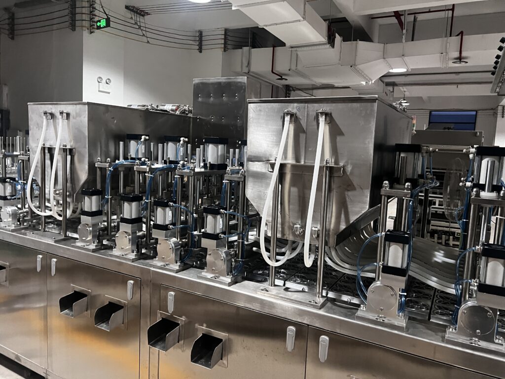 A close-up shot of the multi-head filling nozzles dispensing different colored jelly into butterfly-shaped cups