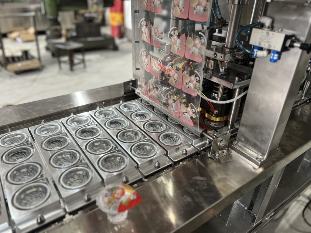 A clear PS plastic cup filled with colorful jelly being sealed on a production line