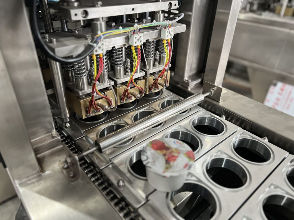 Close-up shot of a paper yogurt cup being sealed by a machine head