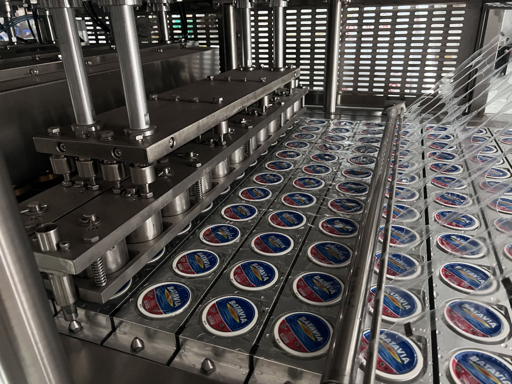A cup filling and sealing machine in operation, filling cups with orange juice