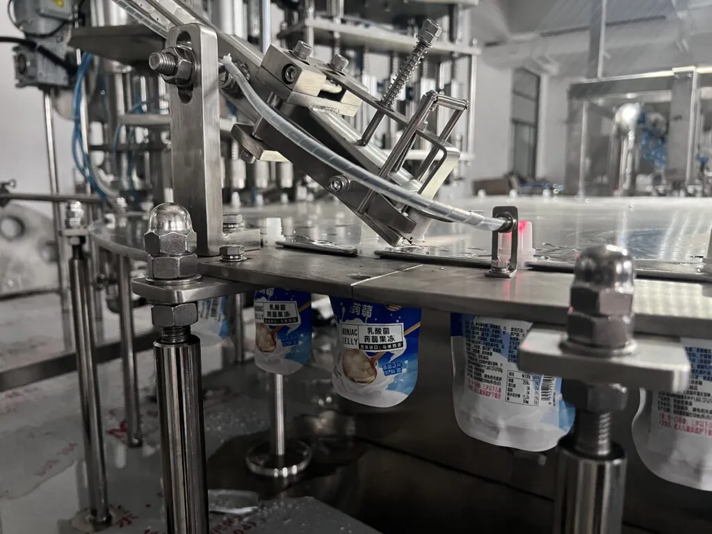 A robotic arm capping a spout pouch on an assembly line