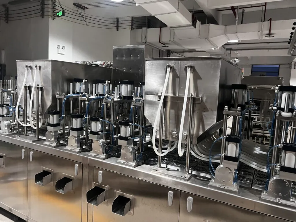 A close-up shot of the multi-head filling nozzles dispensing different colored jelly into butterfly-shaped cups